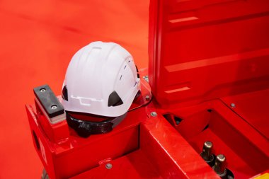 İnşaat ve bakım ortamlarında endüstriyel güvenlik uygulaması kapsamında kırmızı metal ekipman platformunda dinlenen koruyucu beyaz başlık