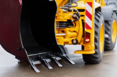 Yüksek çözünürlüklü görüntü bir inşaat yükleyicisinin çelik kovasını ve diş montajını yakalıyor, dayanıklı yapıyı vurguluyor, bileşenleri giyiyor, hidrolik bağlantılar kuruyor.