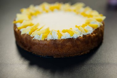 Pürüzsüz krem kaplı ev yapımı peynirli kek ve kenarları koyu arkaplanda derin olmayan dekoratif peynir parçaları.