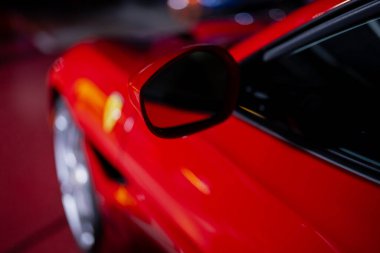 Modern kırmızı spor araba dış detayı yan aynaya ve yansıtıcı boya ile pürüzsüz vücut hatlarına odaklanıyor.