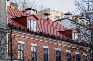 Tarihi tuğla apartmandaki kırmızı metal çatı, konut yenileme, kentsel mimari mirası ve bina bakım endüstrisini gösteriyor.