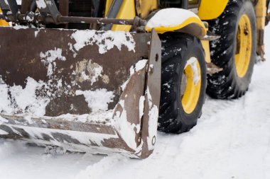 Endüstriyel inşaat ekipmanları, yükleyici kova kenarı ve ağır lastiklerin kısmen açık havada kış mevsiminde karla kaplı olduğu kısımları kaplıyor.