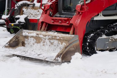 Endüstriyel inşaat makineleri, kırmızı yükleyici kovası ve açık hava kış şantiyesindeki karları temizleyen şezlongları kapatıyorlar.