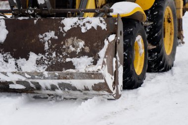 Ön yükleme kovasını kapat ve karla kaplı büyük lastik lastikler kış çalışma koşullarında ağır inşaat makinelerinin çalıştığını gösteriyor.
