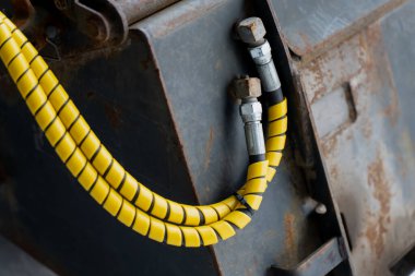 Hidrolik hortum, sarı güvenlik sarmalı ve metal eşleşmeleri içeren endüstriyel makineler. Ağır ekipmanların çelik yüzeyine sabitlenmiş.