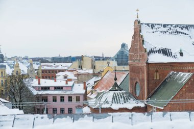 Riga 'nın kar kaplı çatıları, tuğla kilise mimarisi ve yoğun kentsel binaları ile tarihi ufuk çizgisi geleneksel Baltık şehir manzarası oluşturuyor.