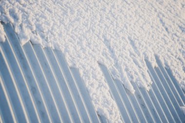 Çelik çatının kıvrımlı tabakasında kar tabakası, tepelerin yakın görüntüsü ve kar kenarları soyut kış dokusu ve inşaat malzemesi arkaplanı oluşturur.