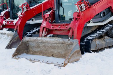 Çoklu kırmızı fren dümeni. Kovaları ve lastik izleri olan inşaat makineleri karda duruyor. Kış mevkii ağır ekipman.