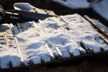 Çelik sürüngen raylarında dinlenen kar, ağır makine pisti ayakkabı ve oluklara yakın, seçici odaklı kış endüstriyel arka planı ve sıcak ışık