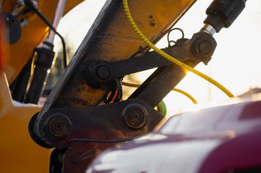 Lobutlar ve hidrolik çalıştırıcı, sarı koruyucu hat ve gün batımında metal bağlantı ile ağır inşaat makinası kol montajı