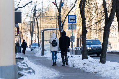 Otobüs durağı barınağı olan Winter City Caddesi, buzlu kaldırımda yayalar ve arka planda trafik, günlük kentsel hareketlilik ve toplu taşıma kavramı