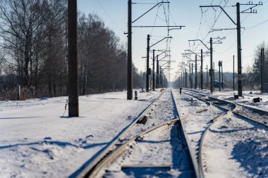 Kış demiryolu kavşağı çoklu karla kaplı, elektrik hatları ve direklerle kaplı, kırsal kesimde gün ışığında perspektif transit rotası