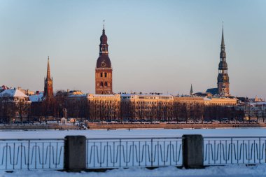 Riga Letonya 'nın katedral kulesi, kilise kulesi siluetleri ve donmuş rıhtım manzarası, açık gökyüzü altında demir parmaklıklar.