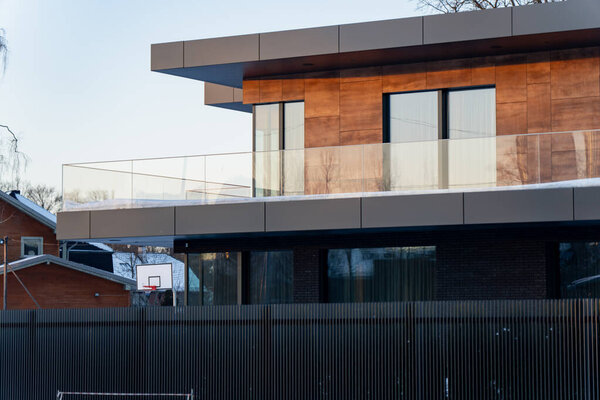 Minimalist modern residence with wraparound balcony, glass balustrade and wood panel cladding, flat roof lines and winter reflections on windows