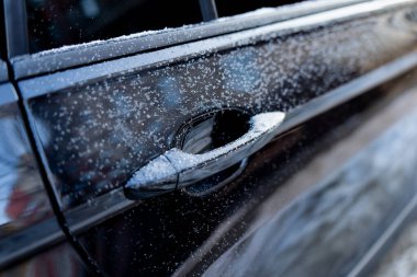 Kar ve buz kristalleriyle kaplı siyah arabanın kapı kolunu kapat. Kış aracı yüzeyinde donmuş damlacıklar ve sığ odak görüşlü yansıtıcı boya var.