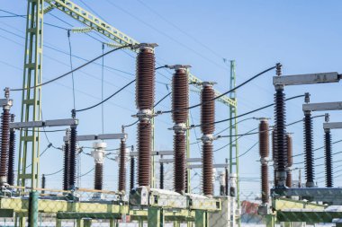 Elektrik iletim santrali, temiz gökyüzü, kamu hizmetleri altyapısı ve enerji tedarik teknolojisi arka planında birden fazla porselen izolatör yığını ve elektrik hatlarını gösteriyor.