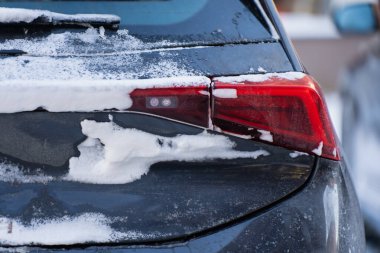 Otomobil arka lambası ve bagaj kapağında kar ve don, yol kiri olan koyu renkli arabada kırmızı arka lambanın detaylı görüntüsü, soğuk mevsim ulaşım teması