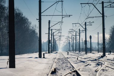 Uzağa uzanan elektrik direkleri, kış ulaşım koridorları ve soğuk mavi ışık altında altyapı perspektifi olan karlı tren rayları.