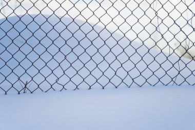 Kışın zincirli tel örgü örgü örülmüş karlar ardında minimalist soğuk mevsim arkaplanı metal elmas desenleri ve yumuşak mavi gölgeleri gösteriyor.