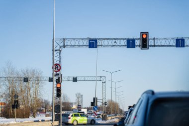 Geniş kış yolu, üstte kırmızı trafik ışıkları, şerit yön işaretleri, ve açık mavi gökyüzü altında bekleyen araçlar.