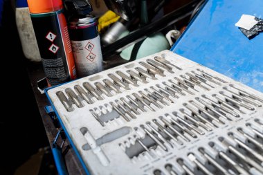 İplik kesme seti ve plastik tepside düzenlenmiş küçük matkap uçları, yakında sprey kutularıyla garajda mavi alet çantası, endüstriyel servis istasyonu ve araç hazırlık teması