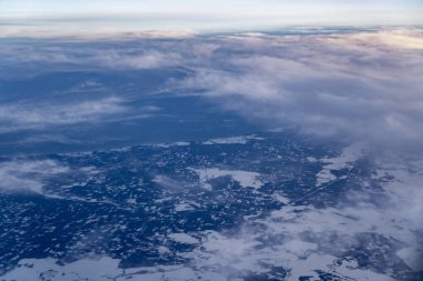 Kırık bulut katmanları, serin mavi tonlar ve seyir yüksekliğindeki yumuşak sis yoluyla görülen karlı arazi ve ormanların hava manzarası coğrafya ve hava durumu temaları için atmosferik uçuş perspektifi