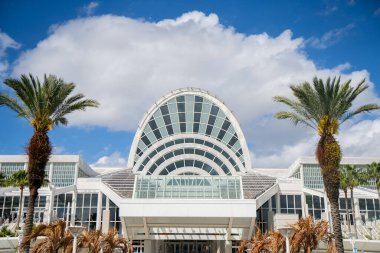 Orlando 'daki Orange County Kongre Merkezi' nin modern mimari cephesi beyaz bulutlu mavi gökyüzünün altında geniş kemerli cam bir girişi var.