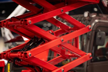 Kırmızı makas kaldırma mekanizması çapraz çelik kollar ve hidrolik parçalar ile kapatılır, araç kiralama, bakım ve endüstriyel erişim temaları için idealdir