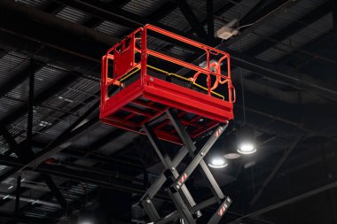 Kiralık temalar, bakım ve müteahhit ekipmanları için uygun koyu metal bir tavanın altında kırmızı bir makas asansörü.