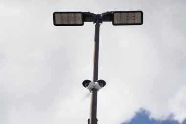 Metal bir direğin üst perspektifinde iki LED lamba ve güvenlik kameraları açık hava ticari bir mülkün üzerine monte edilmiş.