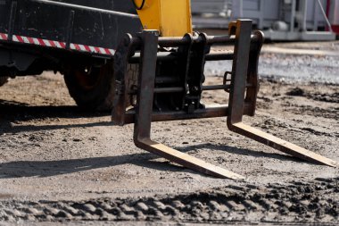 Bir şantiyede ağır ekipman üzerine endüstriyel çatal eklentisi, malzeme taşımacılığı, makine kullanımı ve inşaat alanında modern iş akışını temsil etmektedir.