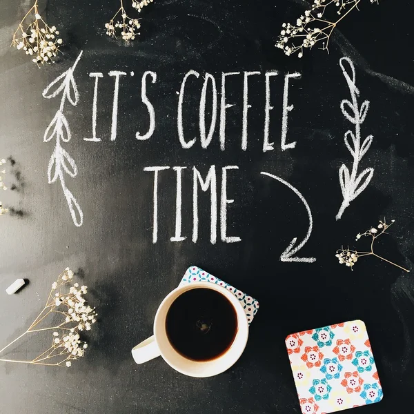 Фраза "Время кофе" написана каллиграфическим стилем на черной доске с белыми цветами и чашкой кофе. Плоский лежал — стоковое фото