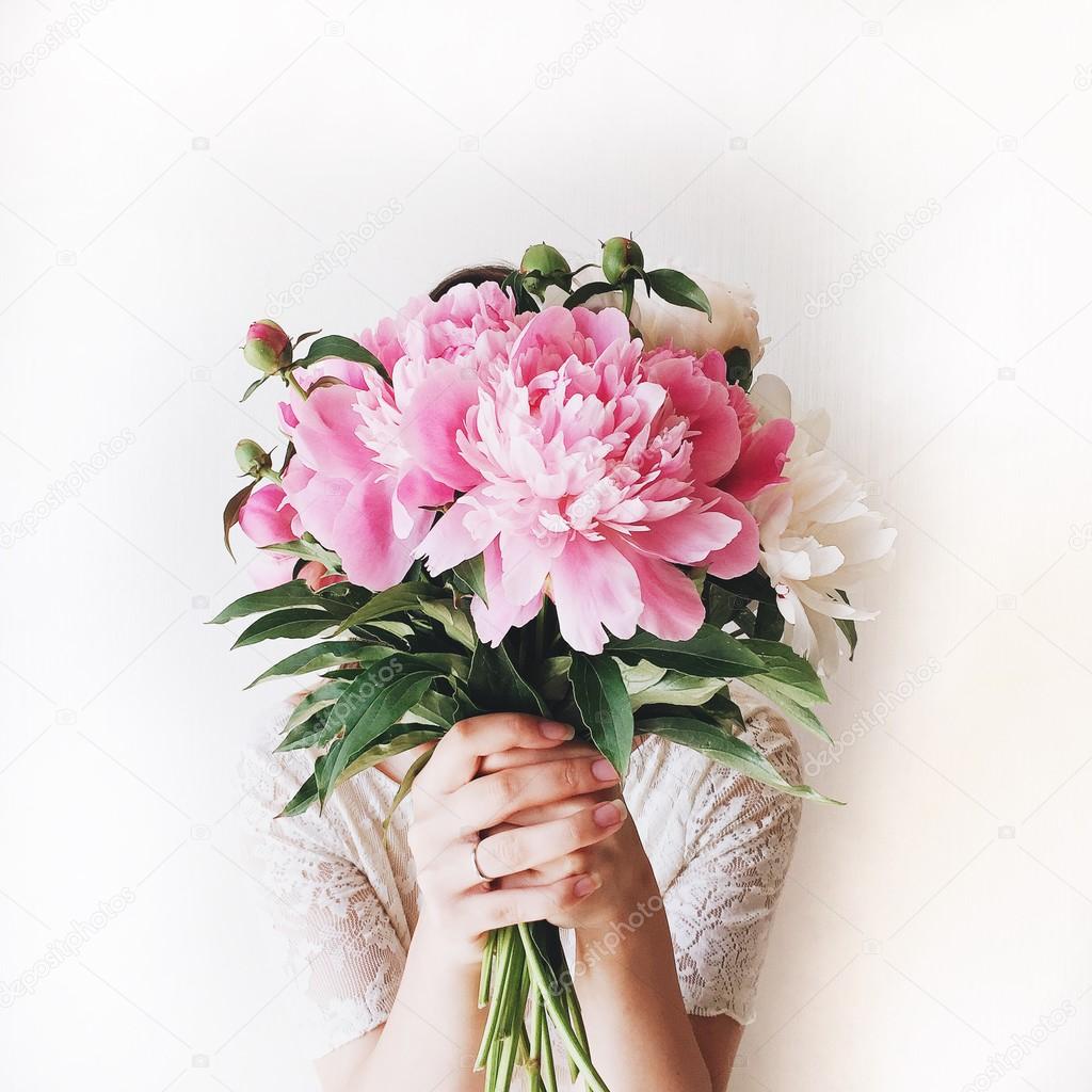 Girl with pink peonies bouquet at white wall