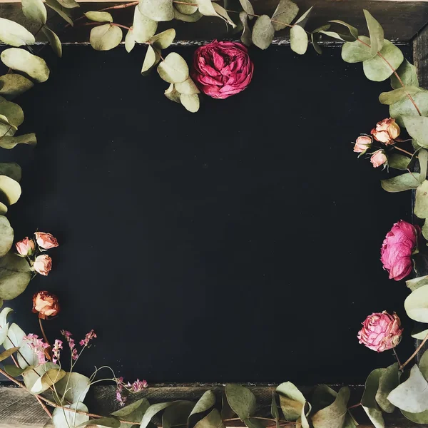 Pembe ve kırmızı güller ve çevresinde yeşil yaprakları ile boş temiz siyah kara tahta. Üstten Görünüm