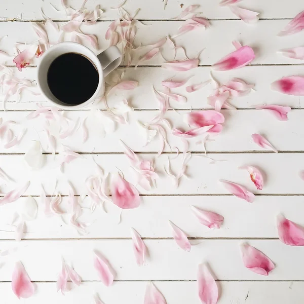 Coupe de café noir et pétales de pivoine rose sur fond de bois blanc. Vue aérienne — Photo