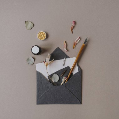 Üzerinde davetiye kartı, kalem, bej arka planda çiçek yaprakları olan düz bir zarf. Düğün davetiyeleri için. Düz yerde, üst tarafta. Blog, web sitesi, sosyal medya için yaratıcı şablon. Moda Paris atmosferi.