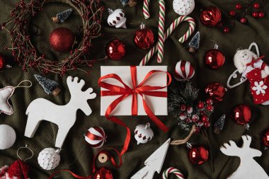 Papyonlu kağıt hediye paketi ve Noel eşyaları: mücevherler, baston şekerler, buruşuk yeşil battaniyeli oyuncaklar. Tatil kutlaması geçmişi. Üst manzara, düz yatış. Noel / Yeni Yıl dekorasyonu.
