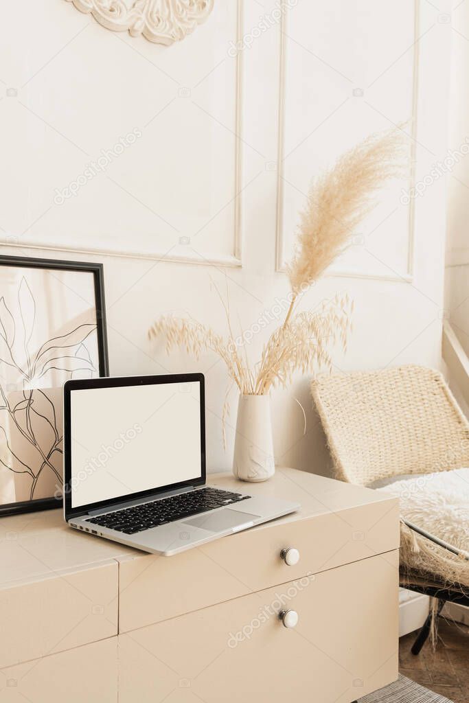 Laptop computer with blank screen on table with boho decorations. Minimal boho styled interior design template with mockup copy space.