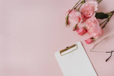 Boş kağıt sayfa not defteri, gül çiçeği buketi, pembe arka planda bardaklar. Asgari ofis masası. Düz yatış, üst görünüm.