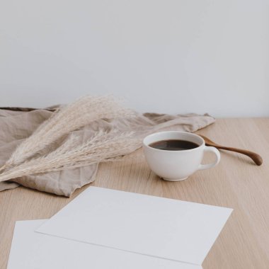 Bej ahşap masada boş kağıt çarşaf. Yıkanmış keten battaniyeli, kahve fincanlı, otlu bir ofis masası. Düğün davetiyesi. Boş kopyalama alanı olan bir model.