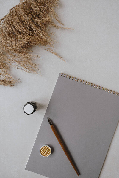 Flatlay blank paper sheet pad, pampas grass, fountain pen, golden ink on beige concrete background. Home office desk workspace. Business, work, lettering, handwriting template. Flat lay, top view.