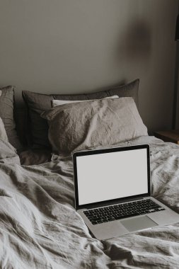 Boş fotokopi alanı olan dizüstü bilgisayar. Modern iç tasarım konsepti. Hygge tarzı yatak odası, gri, yıkanmış çarşaf çarşaflar, yastıklar. Yatak konseptinde asgari çalışma.