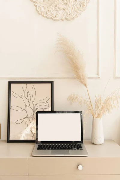 Laptop computer with blank screen pastel beige on table with boho decorations. Pampas grass bouquet, home plant. Minimal boho styled interior design template with mockup copy space.