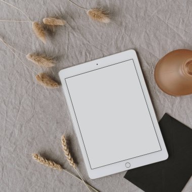 Boş tablet tabletlerin düzlüğü, pofuduk ponpon bitkileri, gri yıkanmış keten arka planda çavdar / buğday kulak sapları. Ofis masası çalışma alanı. İş, iş planı. Düz yatış, üst görünüm.
