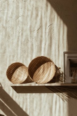 Bohem bohem dekoratif aksesuarlar: fotoğraf çerçeveleri, saman plakalar, beton duvardaki ahşap rafta palmiye yaprağı. Sıcak güneş ışığı gölgeleri duvarda.