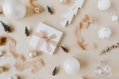 Papyonlu kağıt hediye kutusu ve pastel bej arka planda Noel oyuncakları. Üst manzara, düz yatış. Noel / Yeni Yıl bayramı kutlamaları.