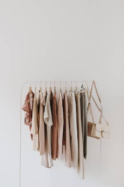 Kadın modası pastel giysileri. Şık kadın bluzları, kazaklar, pantolonlar, kotlar, tişörtler, beyaz arka planda asılı el çantaları. Minimalist moda günlüğü.