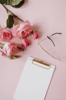 Boş kağıt sayfa not defteri, gül çiçeği buketi, pembe arka planda bardaklar. Asgari ofis masası. Flatlay, üst manzara. Boşluk düzenleme şablonunu kopyala.