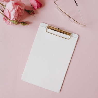 Boş kağıt sayfa not defteri, gül çiçeği buketi, pembe arka planda bardaklar. Asgari ofis masası. Düz yatış, üst görünüm.