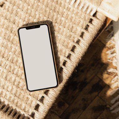 Ratttan sandalyenin üzerinde boş ekran cep telefonu düzlüğü. Düz yerde, üst tarafta. Uzay modelleme şablonunu kopyala. Sıcak güneş ışığı gölgeleri.